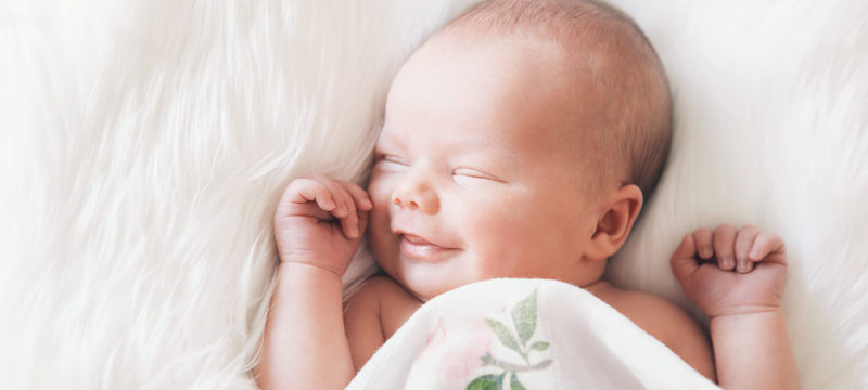 Sleeping newborn baby in a wrap on white blanket.