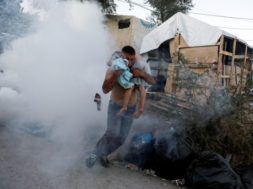 A migrant carries a boy as they flee tear gas fired by riot police during a demonstration, following a fire in Moria camp on the island of Lesbos