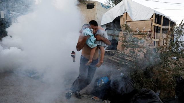 A migrant carries a boy as they flee tear gas fired by riot police during a demonstration, following a fire in Moria camp on the island of Lesbos