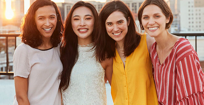Portrait Of Female Friends Gathered On Rooftop Terrace For Party With City Skyline In Background