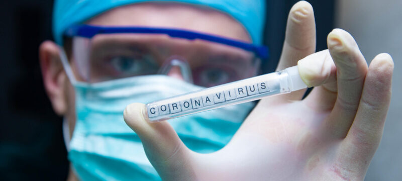 A scientist holds in his hand a test tube with the virus coronavirus.