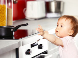 Little child playing with pan and electric stove in the kitchen