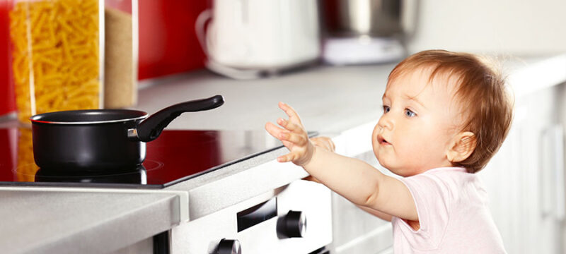 Little child playing with pan and electric stove in the kitchen
