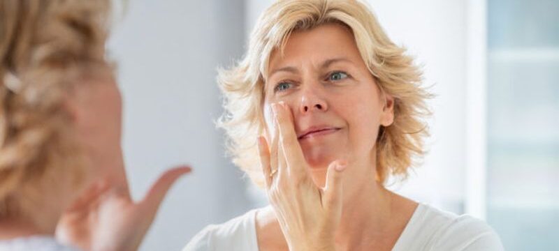 Mid adult woman spreading a layer of facial cream in front of the mirror