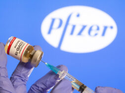 FILE PHOTO: A woman holds a small bottle labeled with a “Coronavirus COVID-19 Vaccine” sticker and a medical syringe in front of displayed Pfizer logo in this illustration