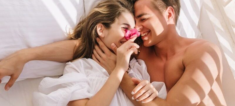 cheerful-young-couple-love-lying-white-bed-enjoying-honeymoon-sunny-morning-smiling-handsome-man-with-bronze-skin-embracing-his-magnificent-girlfriend-vintage-blouse-resting-pillows_197531-3184