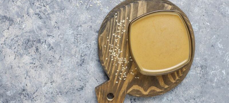 Bowl of tahini with sesame seeds on concrete background