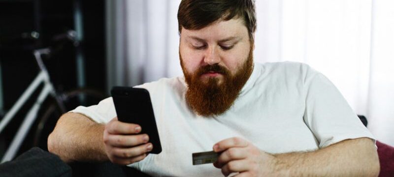 fat-man-types-number-credit-card-his-phone-sitting-couch_8353-5515