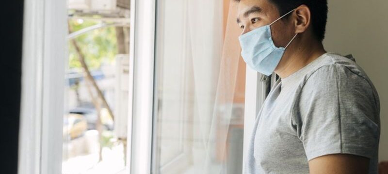 side-view-man-with-medical-mask-home-during-pandemic-looking-through-window_23-2148781390