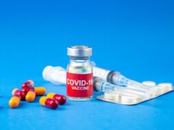front-view-covid-vaccine-ampoules-capsules-packed-pills-syringes-blue-wave-background_179666-19937
