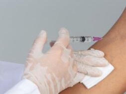 young-doctor-is-injecting-patient-with-hypodermic-syringe-gray-wall_1150-21808