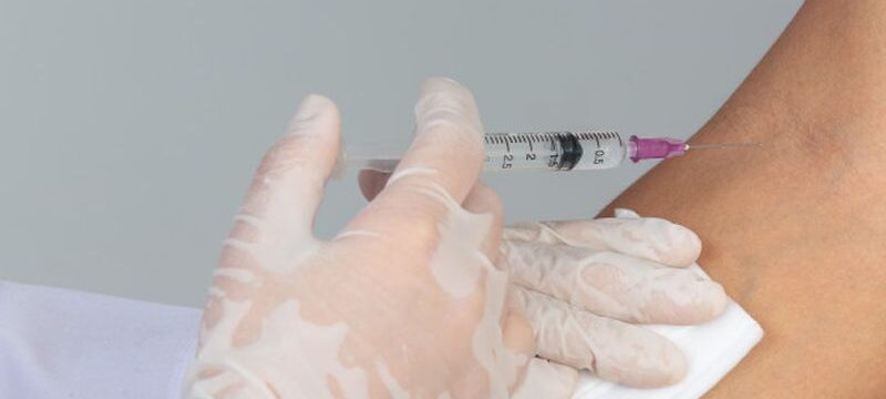 young-doctor-is-injecting-patient-with-hypodermic-syringe-gray-wall_1150-21808