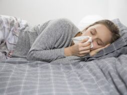Sick woman lying in bed with closed eyes, blowing nose