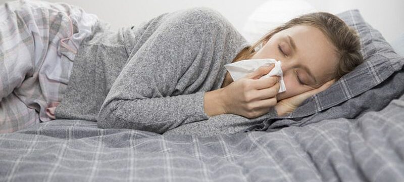 Sick woman lying in bed with closed eyes, blowing nose