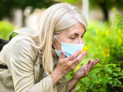 woman-trying-smell-flower-while-wearing-mask_53419-9599