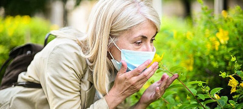 woman-trying-smell-flower-while-wearing-mask_53419-9599
