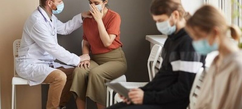 male-doctor-supporting-patient-while-she-crying-they-sitting-corridor-hospital-with-other-people_249974-5230
