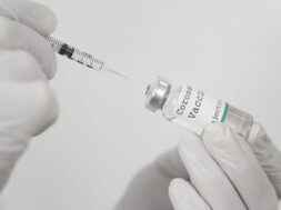 medic-with-latex-gloves-holding-vaccine-vial-syringe_23-2148988293