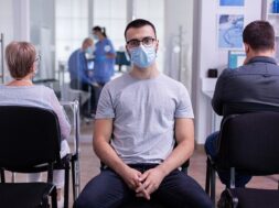 portrait-smiling-young-patient-looking-camera-sitting-chair-waiting-room-hospital-clinic-respecting-social-distancing-while-doctor-working-background_482257-1300