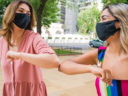 Two friends bumping elbows outdoors.