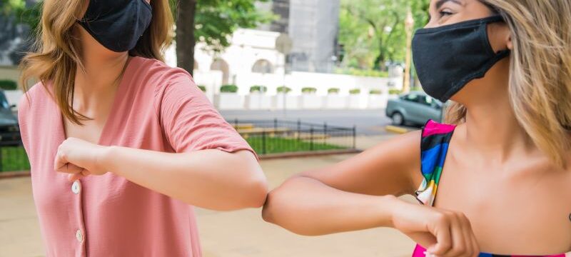Two friends bumping elbows outdoors.