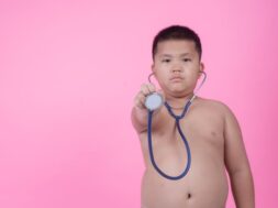 Obese boy who is overweight on a pink background.