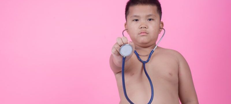 Obese boy who is overweight on a pink background.