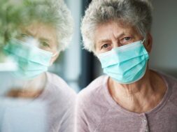 a old woman or grandma is wearing a respirator or surgical mask and looking out of the window
