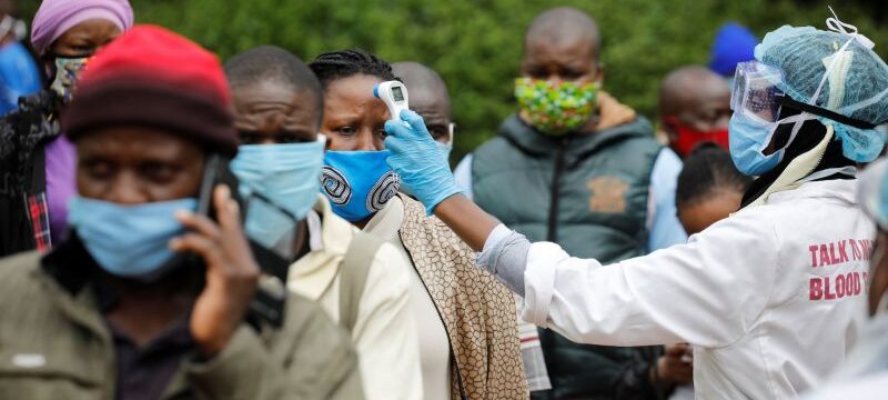 A health worker takes the temperature of a person standing in line for mass testing in an effort to stop the spread of the coronavirus disease (COVID-19) in the Kibera slum of Nairobi