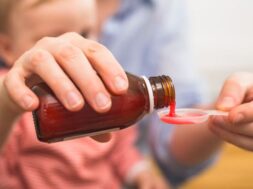 close up of mother pouring cough syrup. blurred baby boy in back
