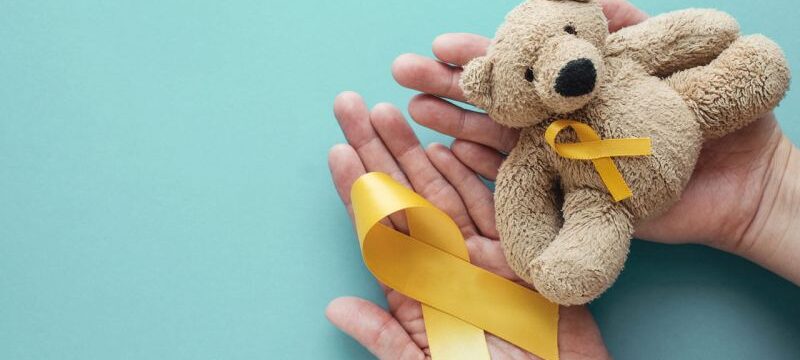 Hands holding children soft toy brown bear with yellow gold ribb