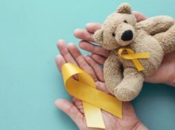 Hands holding children soft toy brown bear with yellow gold ribb