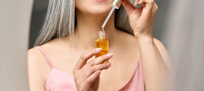 Closeup cut shot of mature Asian woman holding pipette and bottle serum.