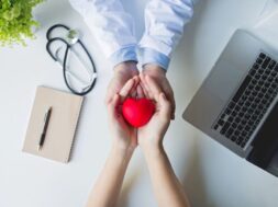 top-view-doctor-patient-hands-holding-red-heart-white-table (1)