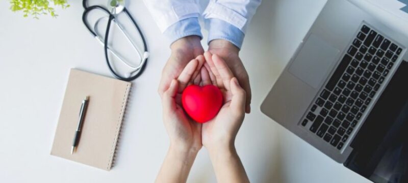 top-view-doctor-patient-hands-holding-red-heart-white-table (1)