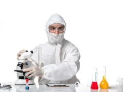 front-view-male-doctor-protective-suit-with-mask-due-covid-using-microscope-light-white-space