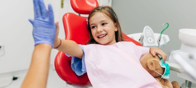 Cute little girl sitting on dental chair and having dental treatment.