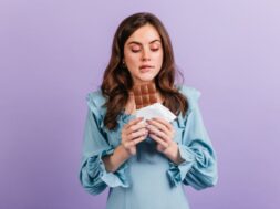 Portrait of funny brunette woman biting her lip in anticipation of tasty lunch. Girl in blue dress looks at delicious chocolate.