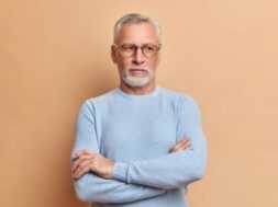 Thoughtful old grey haired grandfather keeps arms folded and looks away pensively ponders over something important dressed in casual jumper being deep in thoughts feels lonely as lives alone