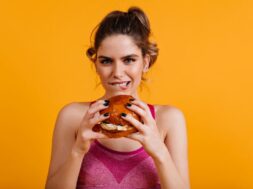 Adorable young lady eating burger. Indoor portrait of girl with big sandwich