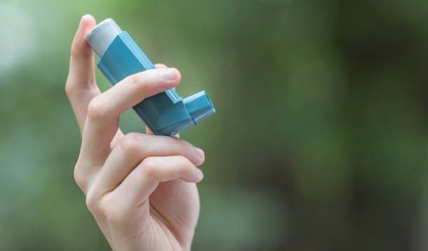 View of a man’s hand holding a blue asthma inhaler
