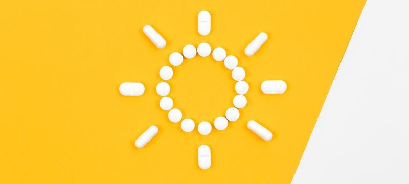 Pills in the shape of the sun, on a yellow background, flat lay.