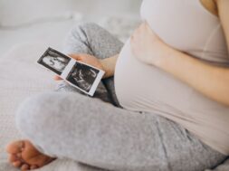 Pregnant woman with ultrasound photo sitting on bed