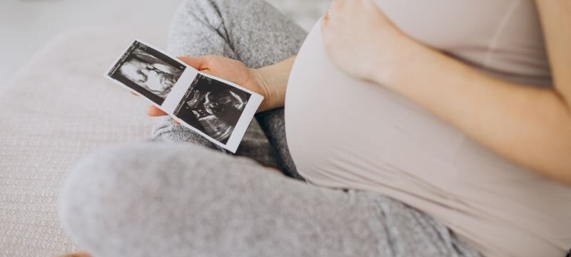 Pregnant woman with ultrasound photo sitting on bed
