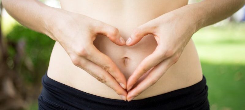 Close-up of female hands shaping heart on belly