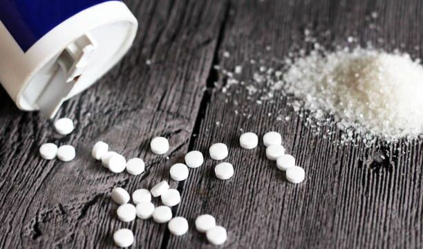Sweetener tablet and sugar on wooden background, food