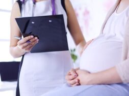 Young woman doctor with stethoscope and tablet speaking with pregnant woman at hospital.