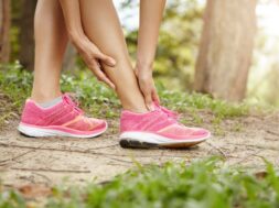 Running sport injury. Female athlete jogger wearing pink sneakers touching her twisted or sprained ankle while jogging or running outdoors. Woman runner massaging her calf muscle before workout