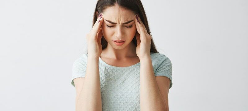 Young beautiful brunette girl frowning touching temples. Headache. Isolated on white background.