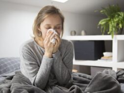 Sick woman sitting in bed, blowing nose with napkin